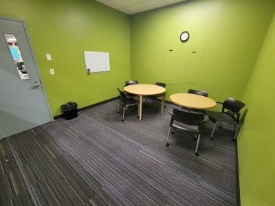 Small meeting room with two round tables, a whiteboard, six chairs.