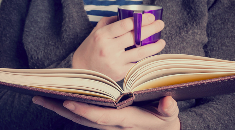 Person reading book with purple mug