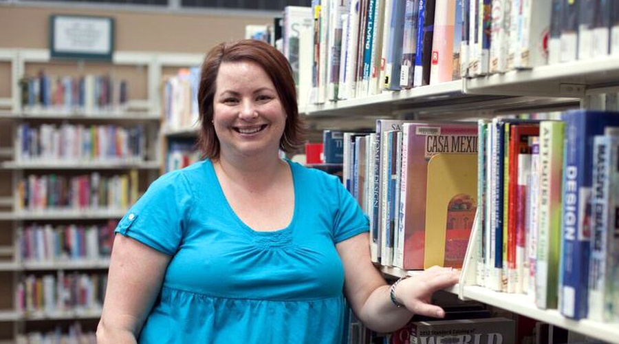 Woman smiling with hand on bookshelf