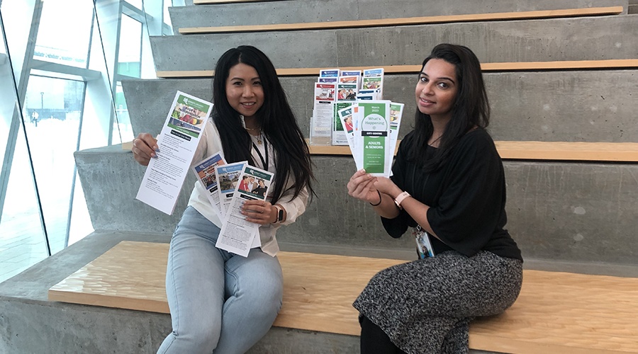 Two staff members holding paper low cost services brochures.