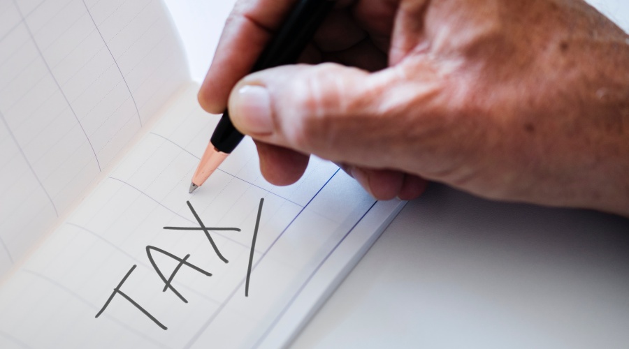 Hand holding pen with word tax written on paper