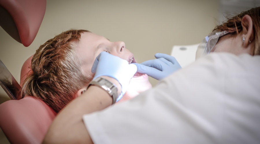 Young boy in dentist chair with dentist flossing his teeth