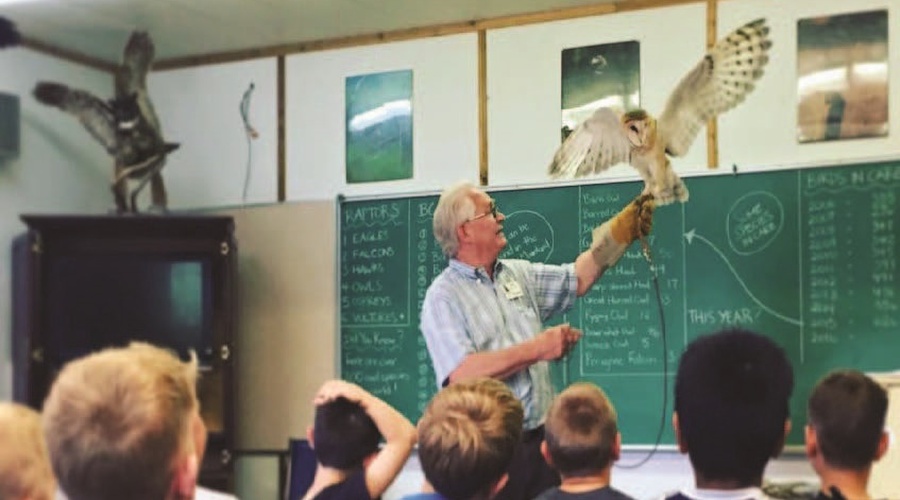 Man holding an owl in front of a classroom full of children