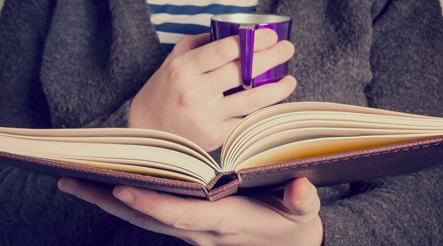 Person holding coffee mug and book