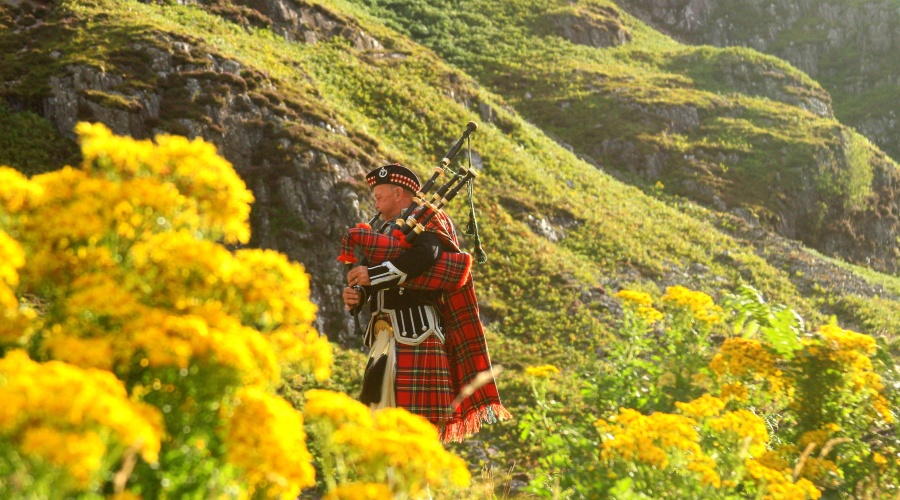 Bagpiper in tartan outside on a hillside