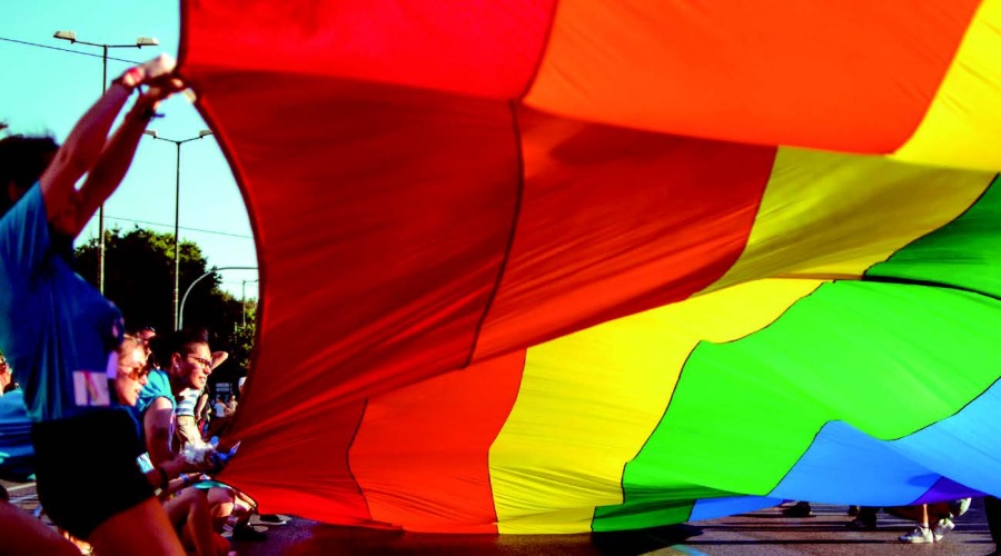 Group of people holding a very large rainbow coloured flag