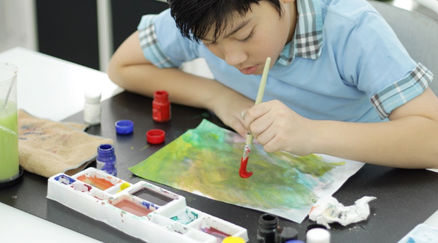Teen focussed on painting, seated at a table.