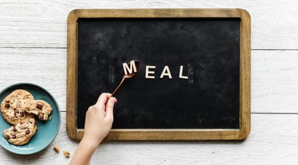 Letters spelling meal, hand with spoon and plate of cookies