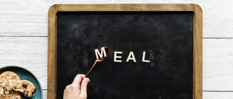 Letters spelling meal, hand with spoon and plate of cookies