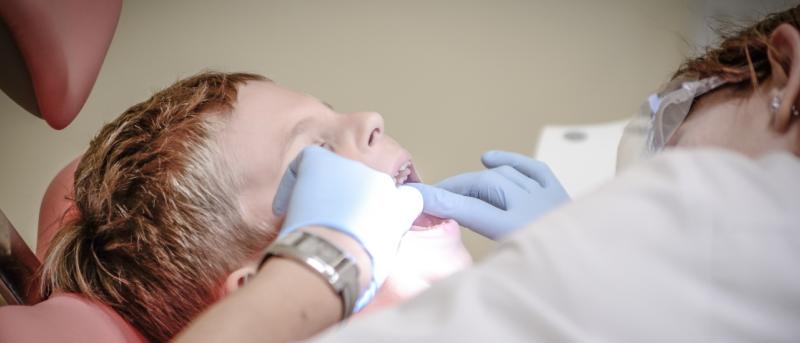 Young boy in dentist chair with dentist flossing his teeth