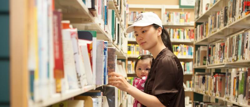Woman holding baby and looking for books