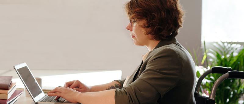 Woman in wheelchair using laptop with stack of books